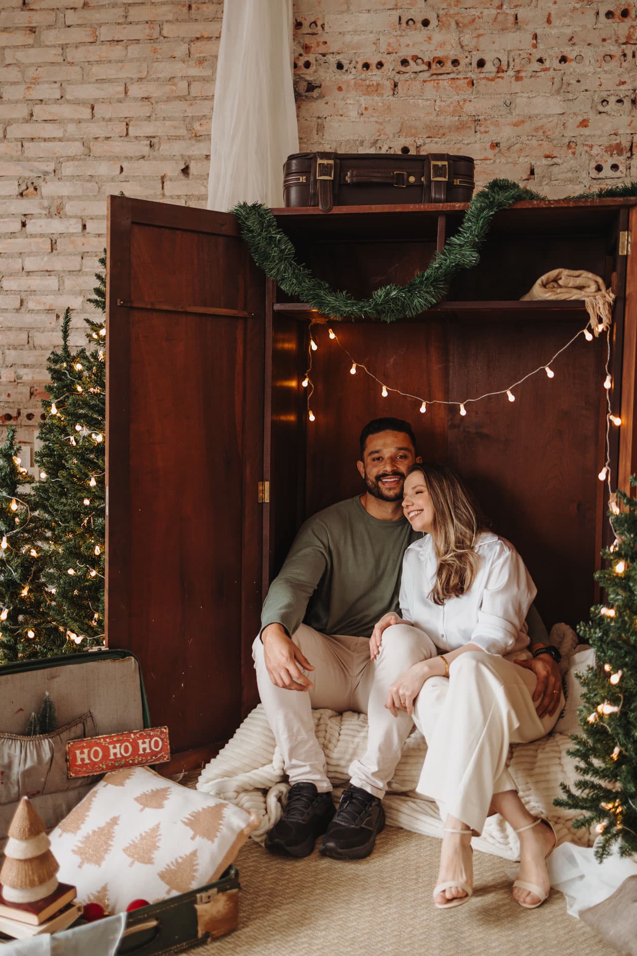 Casal sentado no armário rústico iluminado com Ho Ho Ho e malas