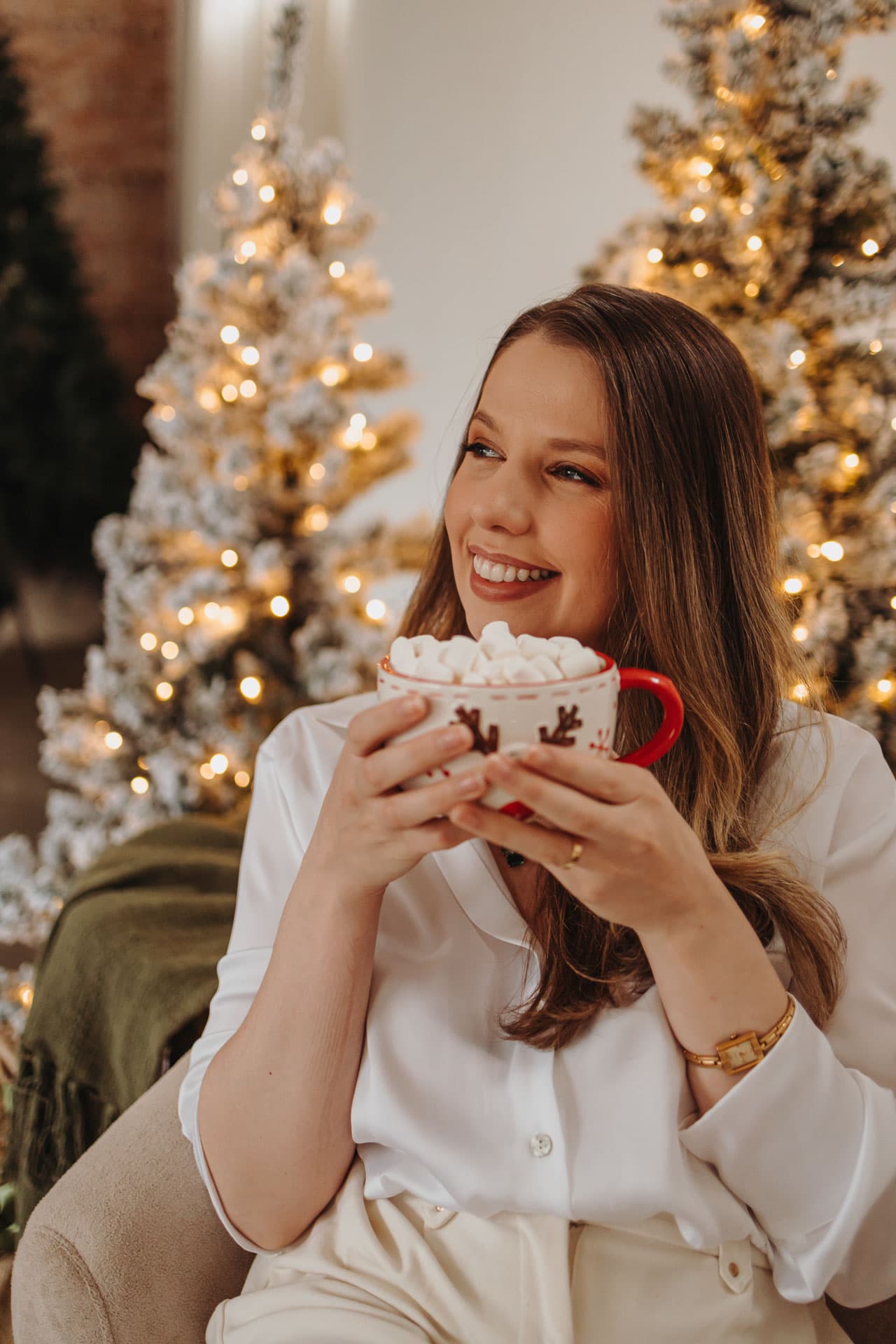 Mulher sorrindo com caneca de marshmallows na árvore iluminada